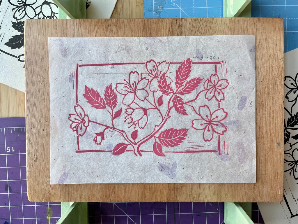 Linocut print of a cherry blossom branch in pink ink on decorative petal paper.